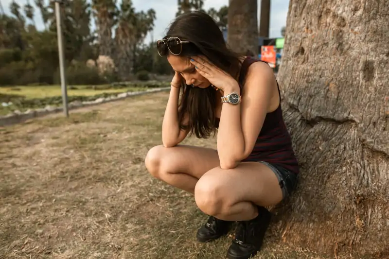 Attacco di panico sintomi fisici: giovane donna ai piedi di un albero con le mani sulle tempie che manifesta i sintomi tipici del panico (Foto di Rodnae Productions da Pexels)