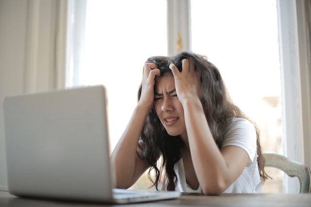 Stress sintomi: volto di ragazza con evidenti sintomi di stress lavoro correlato e seduta al tavolo con le mani tra i capelli