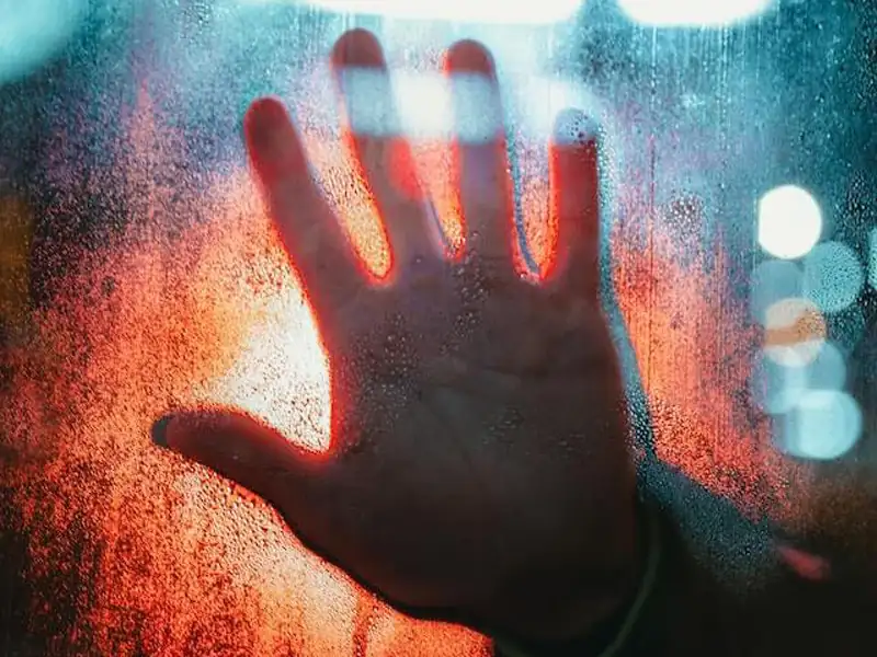Sindrome dell'impostore sintomi: foto di una mano appoggiata su un vetro, quasi ad indicare l'esclusione da un luogo